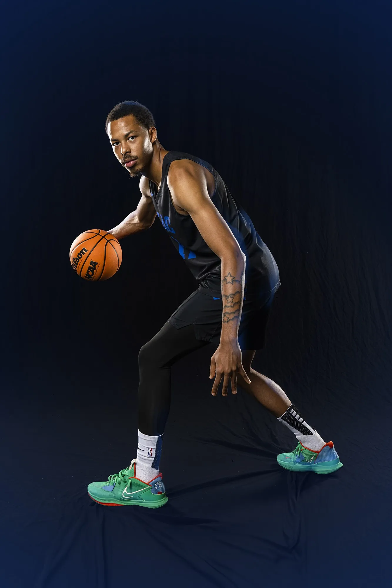 A basketball player holds the ball in a dark studio.