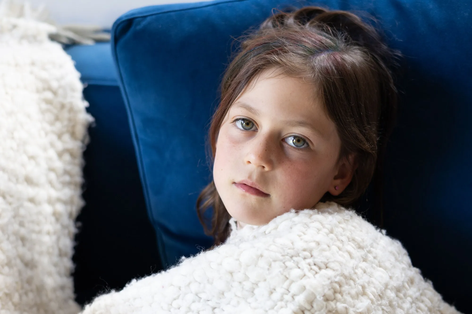 A child rests on a blue sofa beneath a soft white blanket.