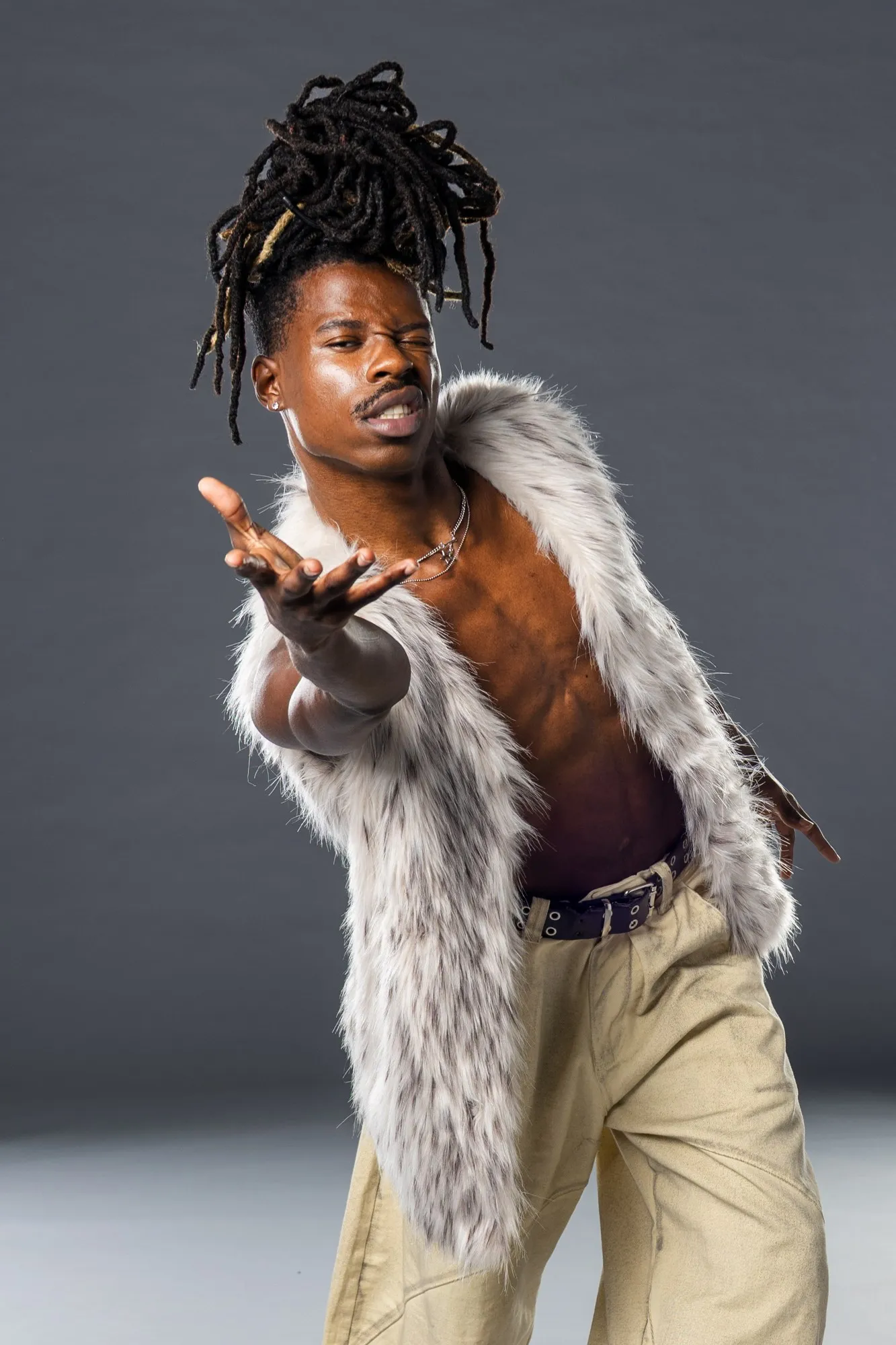 A fashion portrait shows a model in a feathered vest against a gray background.