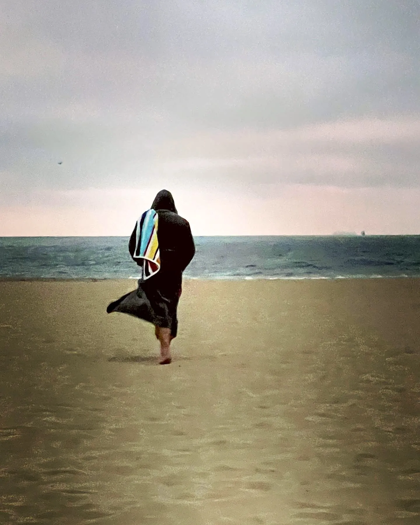 A lone figure stands where the beach meets the water.