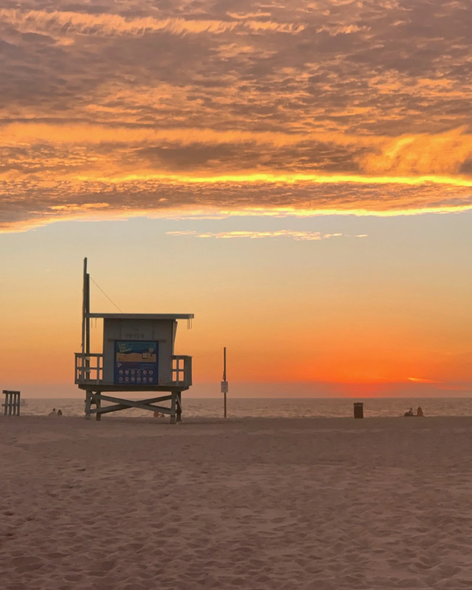 A lifeguard tower silhouetted beneath layers of gold clouds