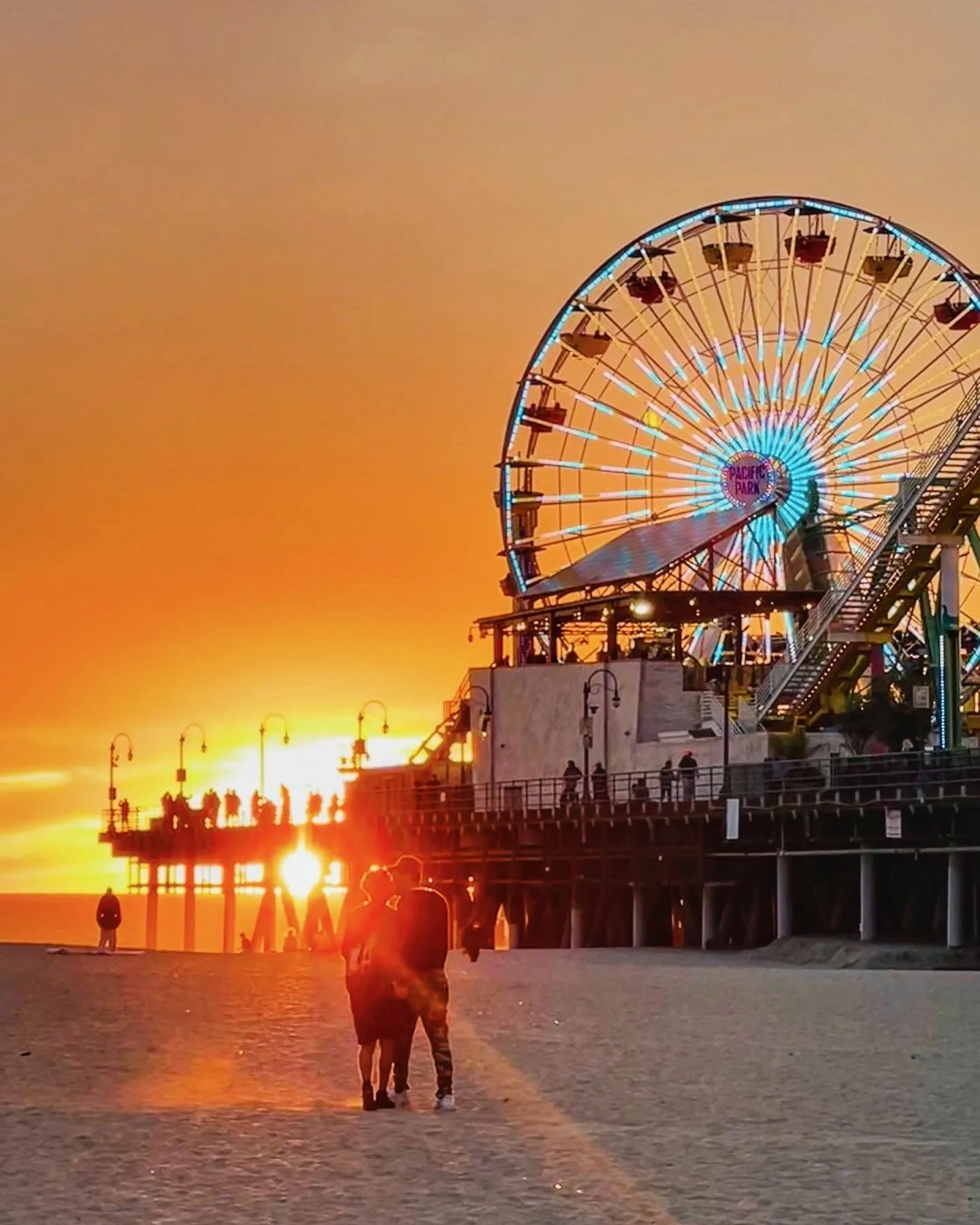 A Ferris wheel silhouetted beside the low orange sun