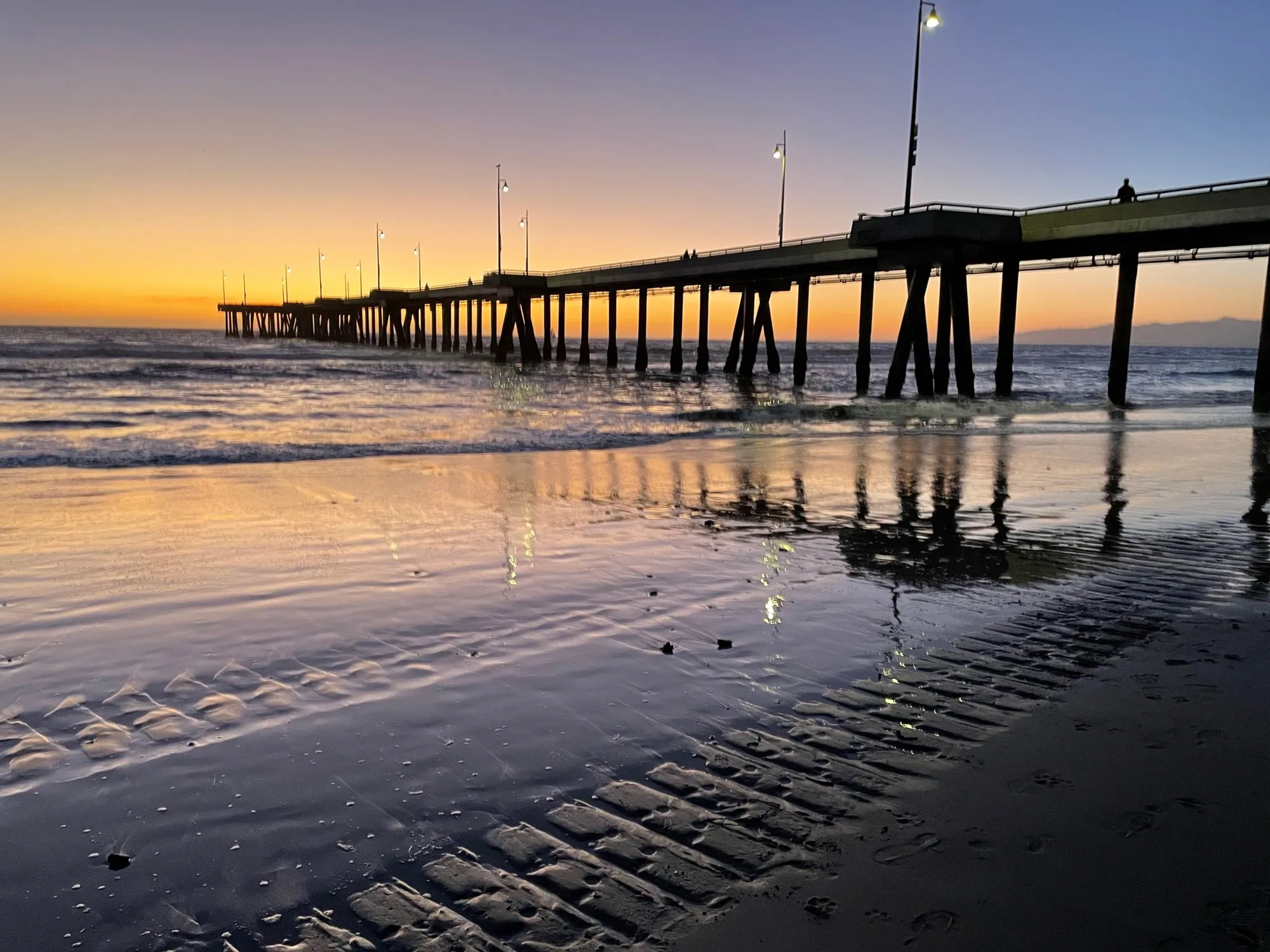 A low pier stretches across the horizon beneath a luminous apricot sunset.