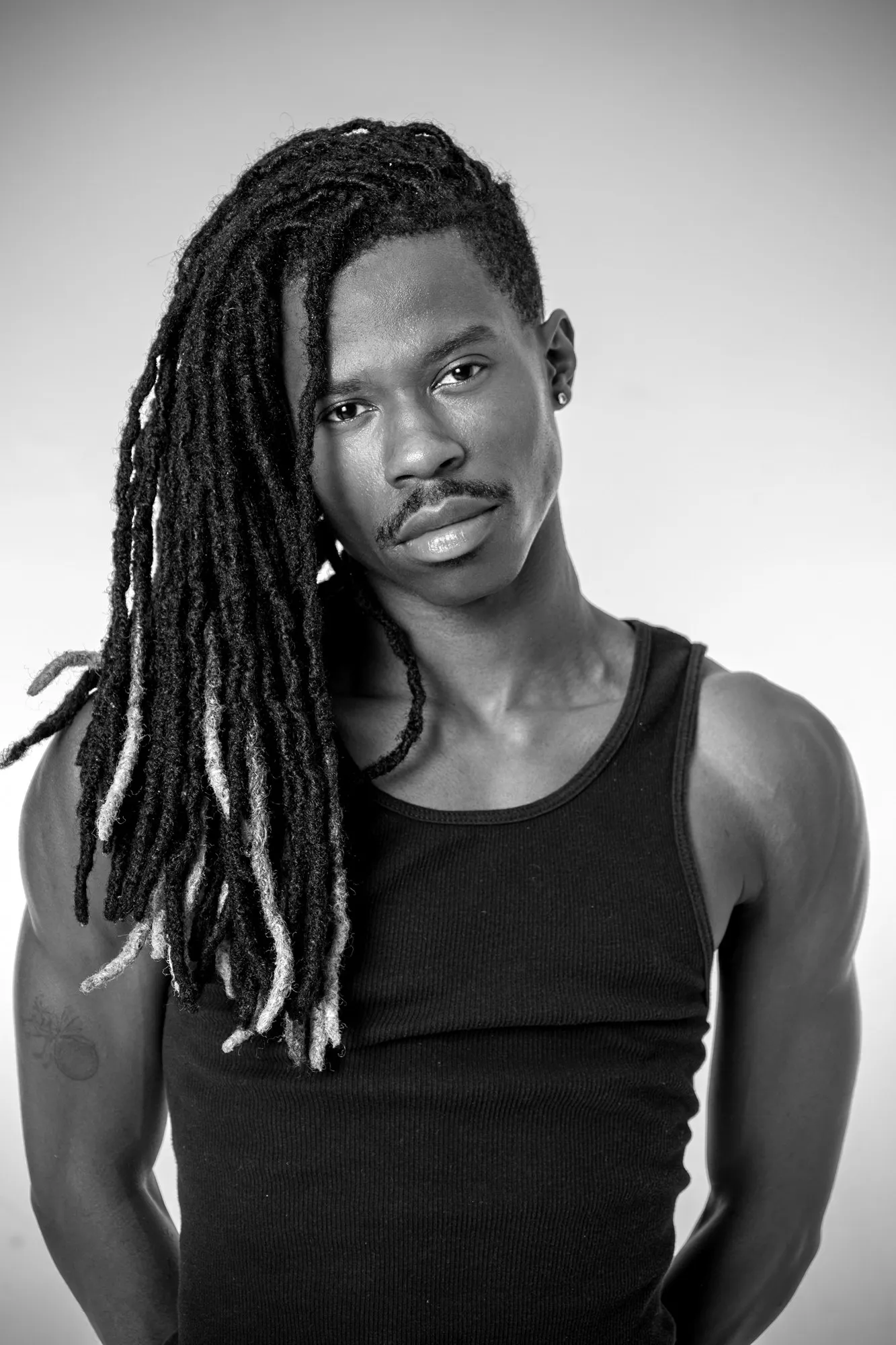 A man with long locs poses in a black-and-white portrait.