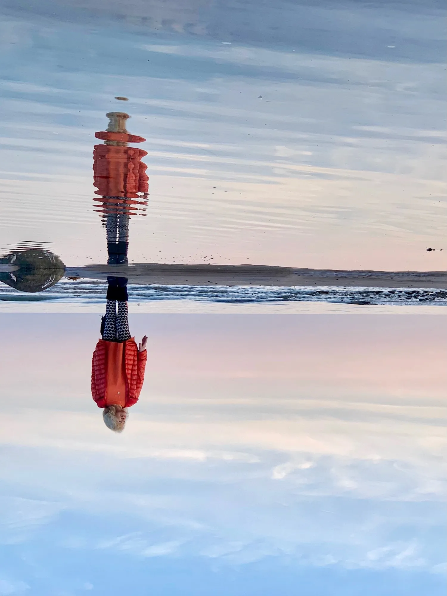 An inverted composition of a person in an orange jacket and their rippling reflection