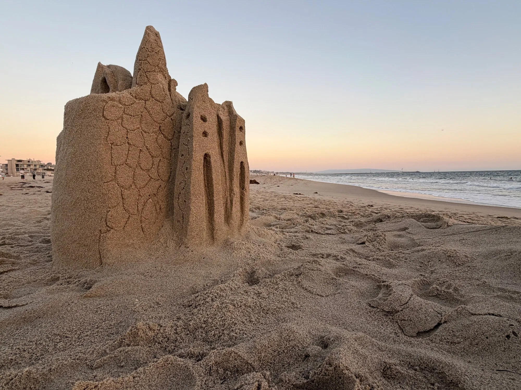 A detailed sandcastle standing beside a quiet shoreline at dusk