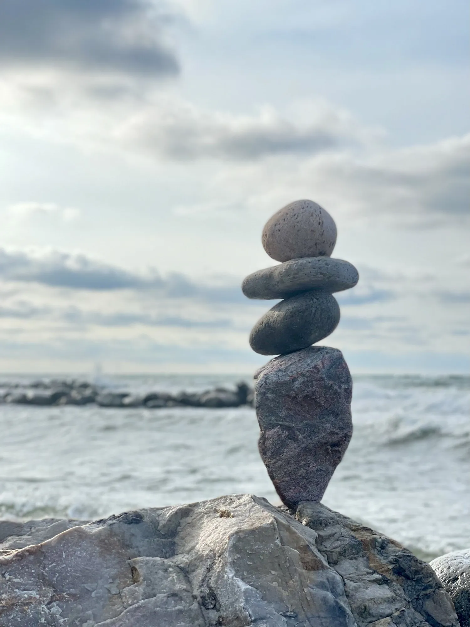 A pale stone stack stands against the subdued colors of a cloudy shoreline.