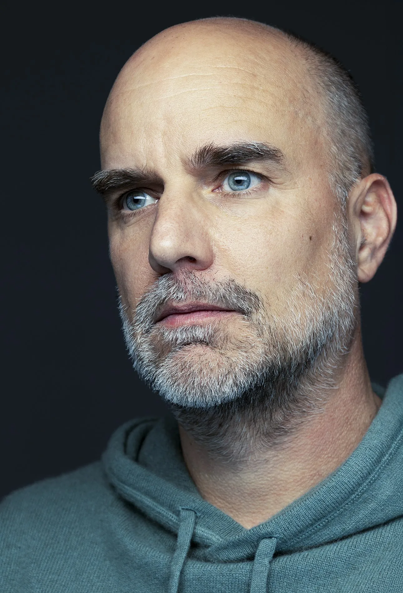 Close portrait of a bald man looking to the side against a dark background