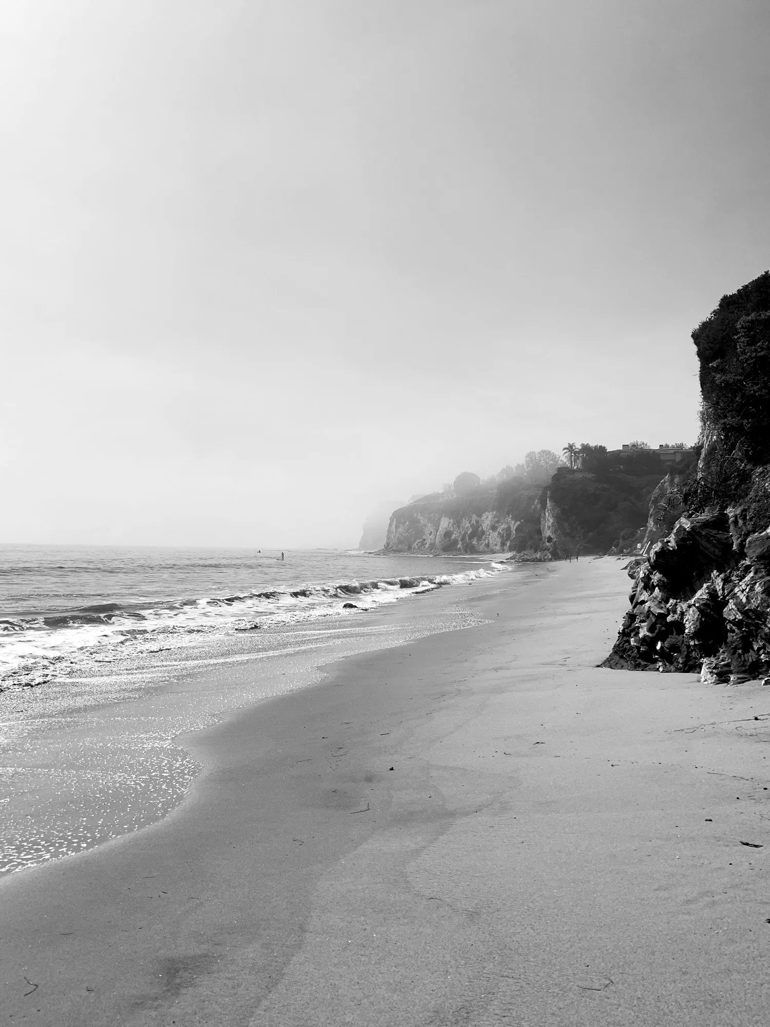 A quiet black-and-white coastline beneath hazy cliffs