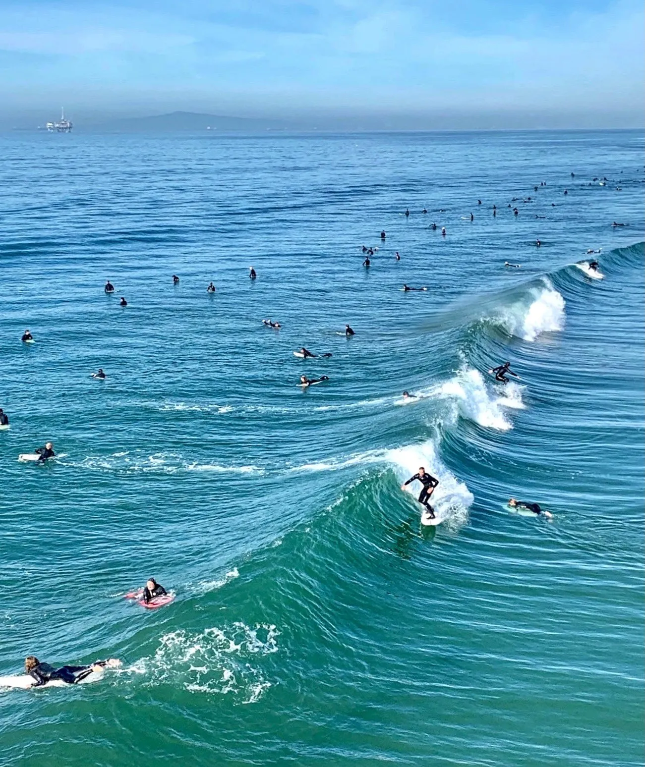 Long blue ocean waves with surfers seen from above