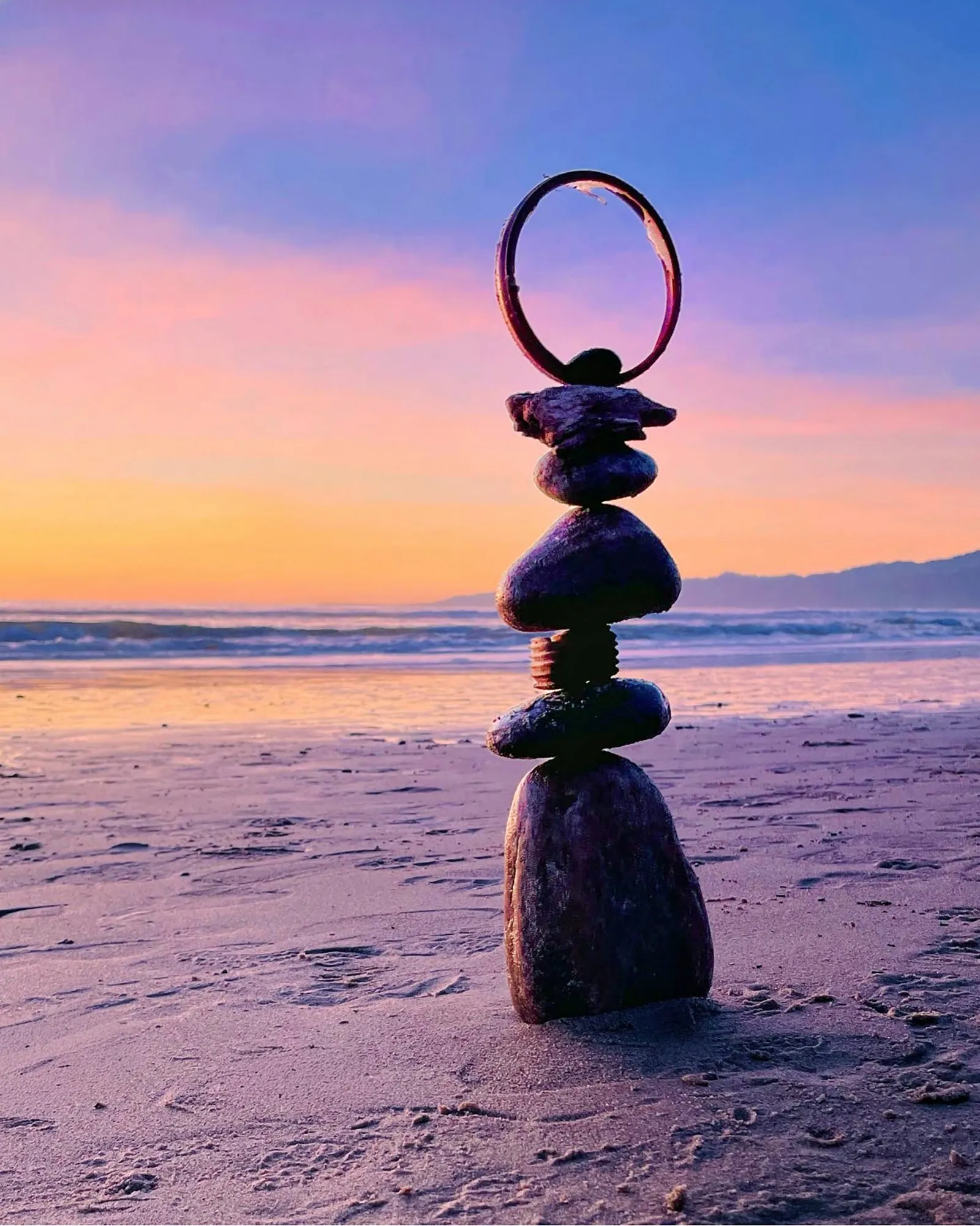 A circular loop balanced above a stone tower against a pink and violet sky