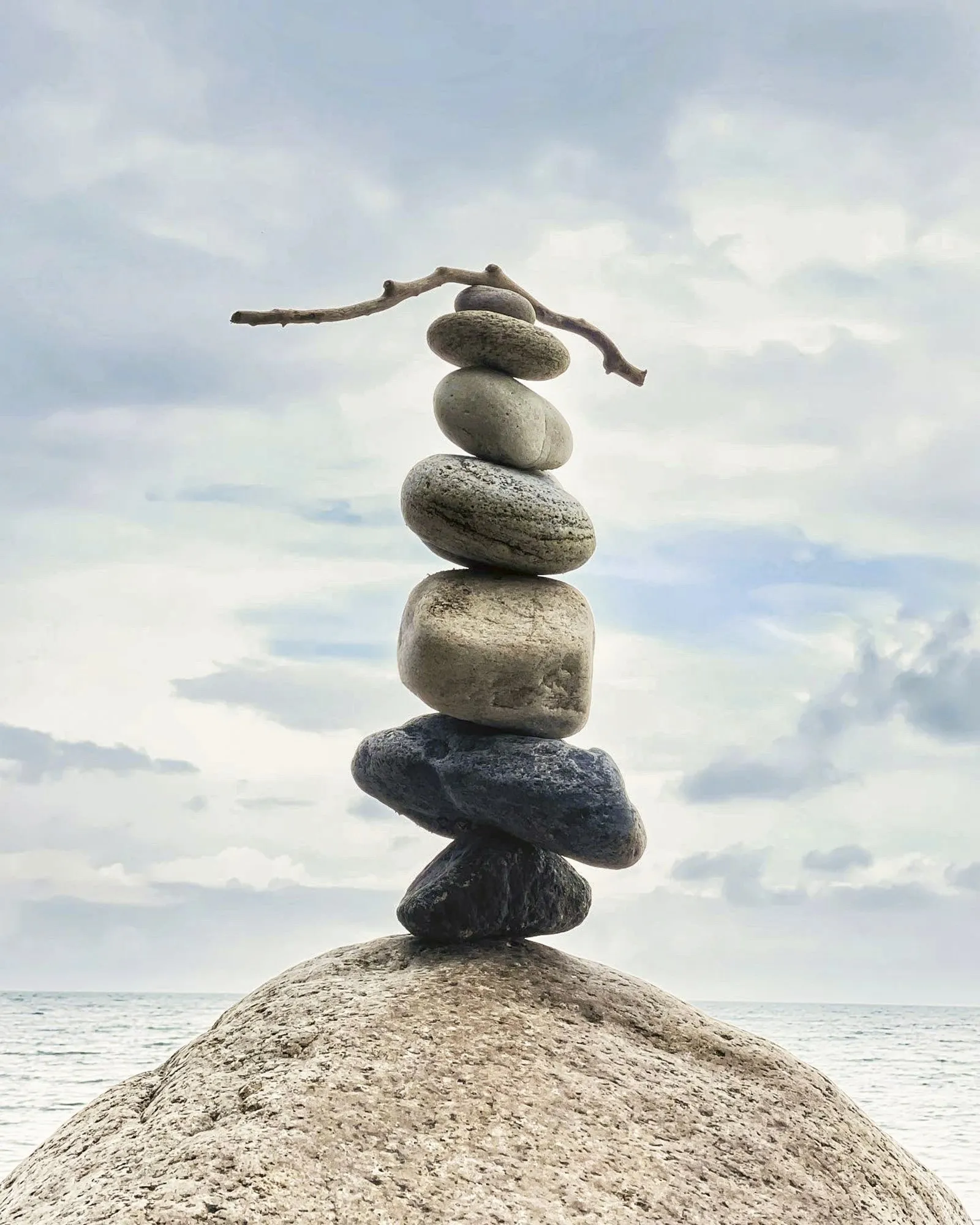 A pale stone tower with driftwood balanced at the top beside the ocean