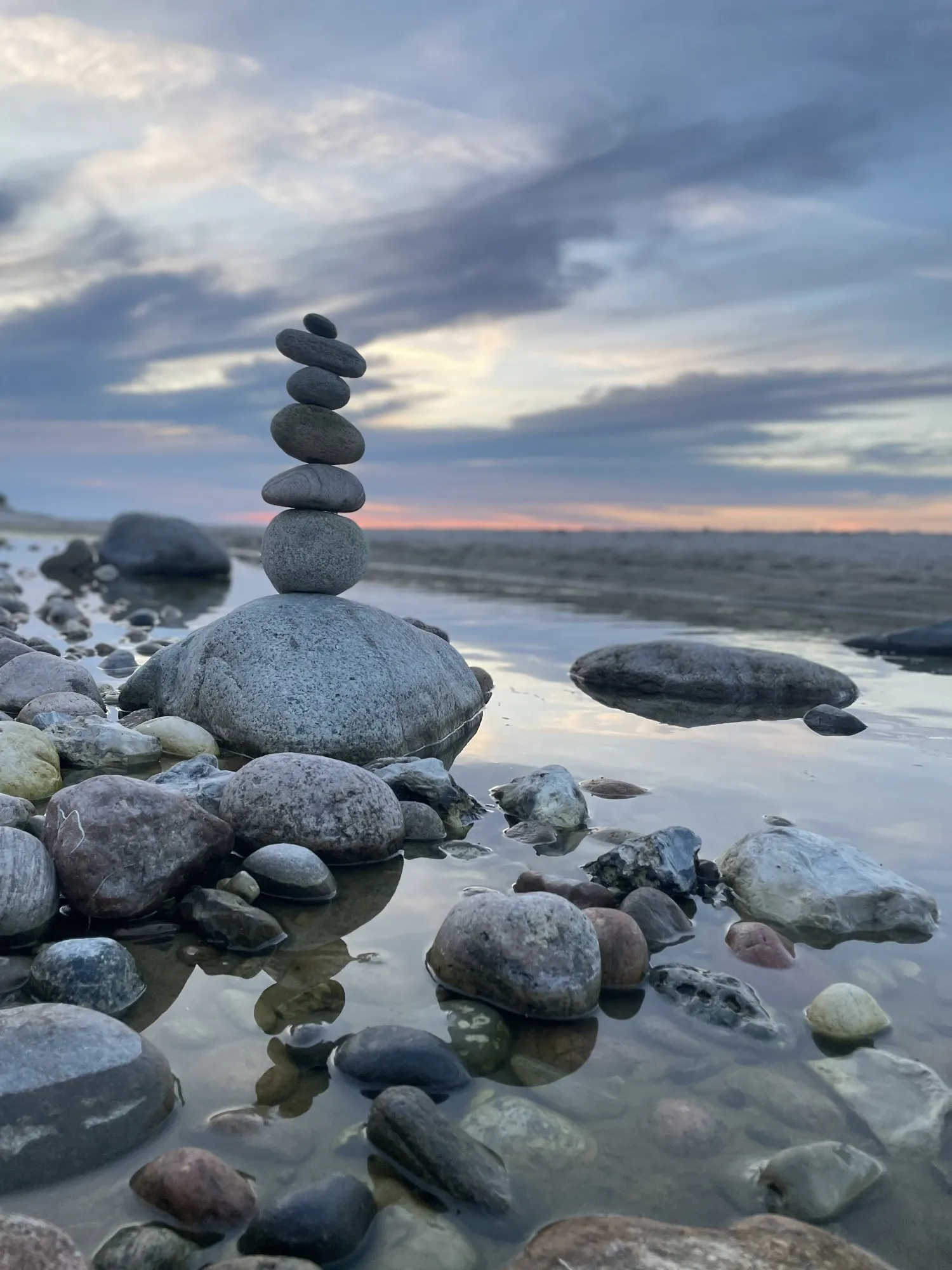A pale stone stack on the rocky shoreline beneath a sweeping clouded sky