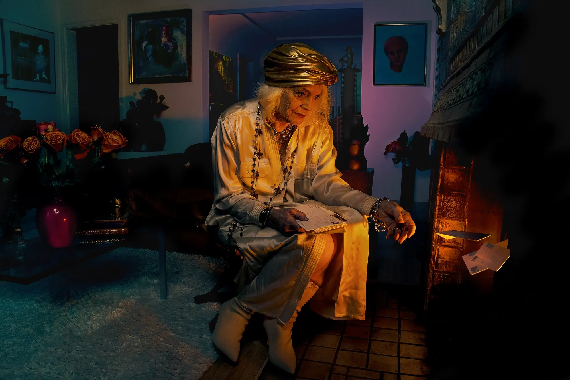 A seated woman in a warmly lit, colorful interior looks down thoughtfully.
