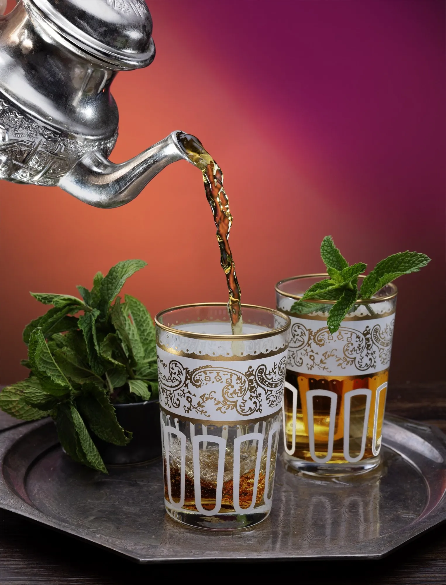 A stream of water pours from a sculptural metal spout into a clear glass.
