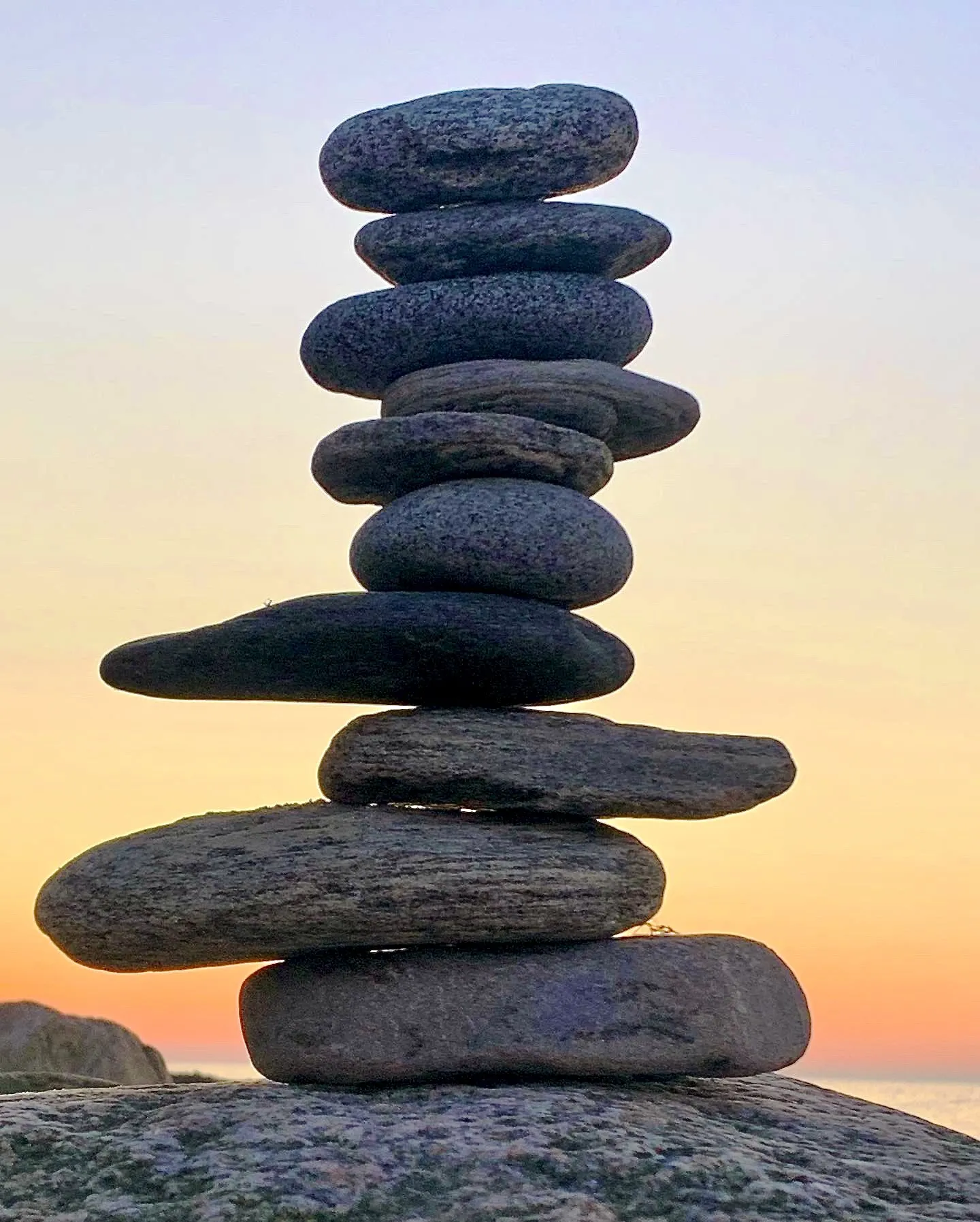 A tall stack of dark stones is silhouetted against a peach sunset.