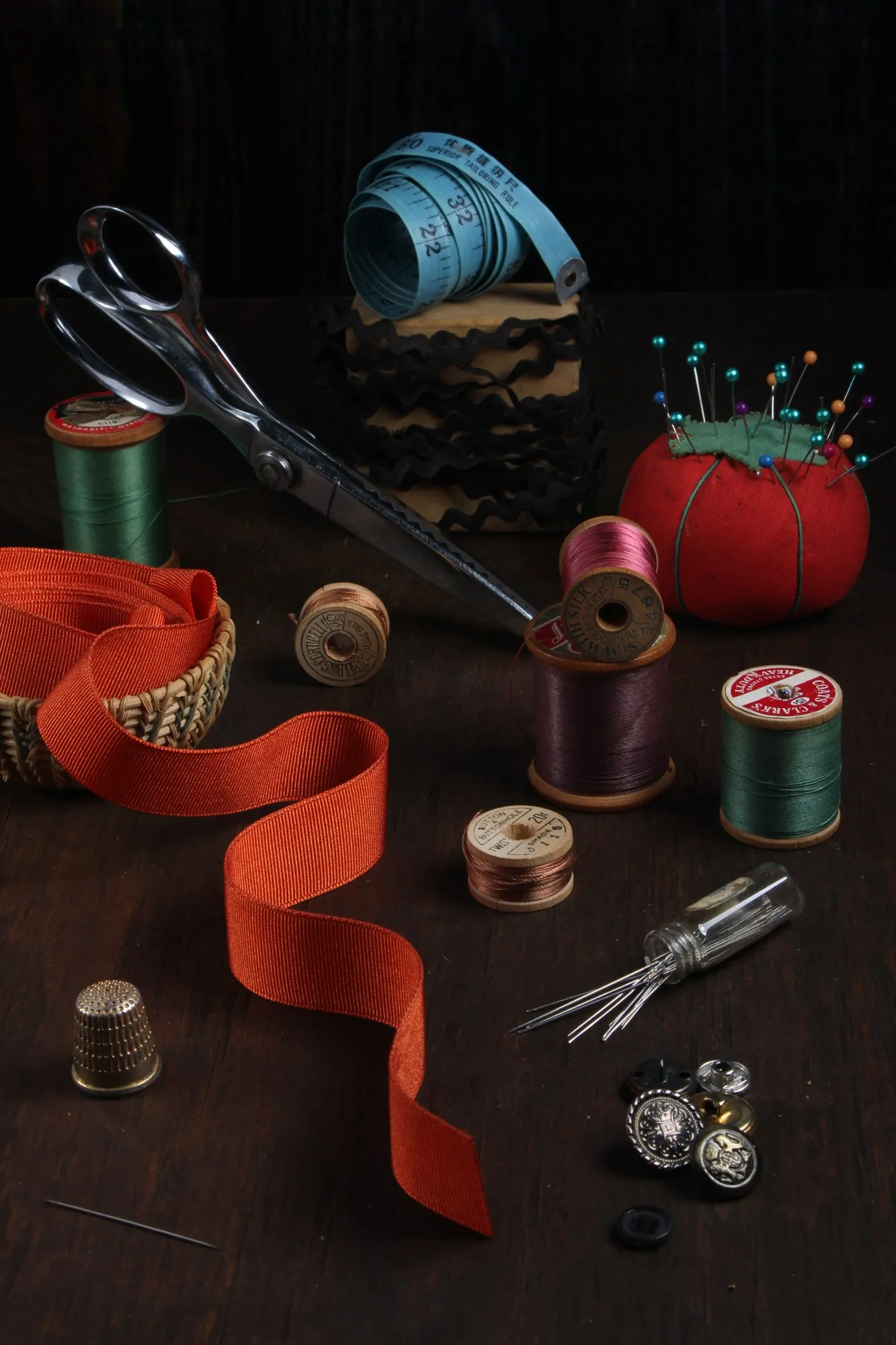 Thread spools and red ribbon are arranged in a warmly lit sewing still life.