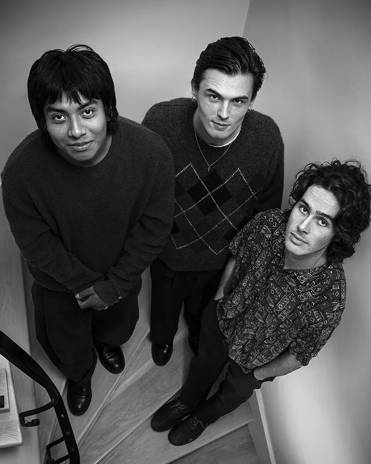 Three friends lean toward the camera in a black-and-white group portrait.